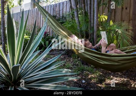 Une mère et son petit garçon sont dans un hamac et lisent un livre d'images ensemble dans leur cour luxuriante à Miami, en Floride. Banque D'Images