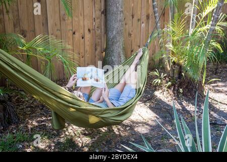 Une mère et son petit fils sont dans un hamac et lisent ensemble un livre d'images dans leur arrière-cour à Miami, en Floride. Banque D'Images