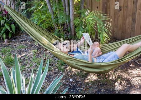 Une mère est avec son petit garçon dans un hamac et a lu un livre d'images ensemble dans leur arrière-cour à Miami, en Floride. Banque D'Images