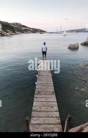 Homme debout sur une jetée en bois, au crépuscule, dans un cadre paisible. Mâle touristes se tient sur un quai en bois à Porto Rafael, Costa Smeralda, Sardaigne, Italie Banque D'Images