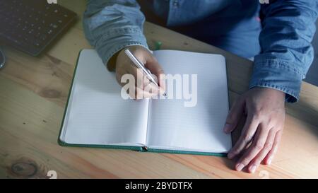 Un homme anonyme est studing et écrit dans un carnet sur le bureau de travail la nuit. Personne écrit une lettre. Rédacteur. Formation Banque D'Images