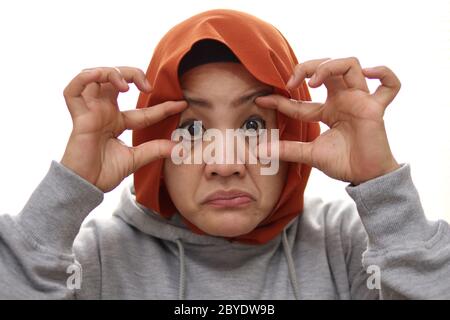 Une femme musulmane fatiguée ouvre les yeux avec le doigt, essayant de rester éveillée, portrait de près isolé sur blanc Banque D'Images