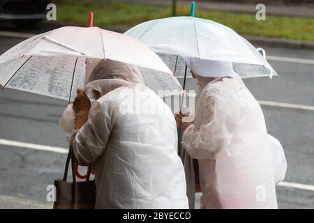 Deux femmes portant des ponchos et des parasols blancs assortis. Banque D'Images