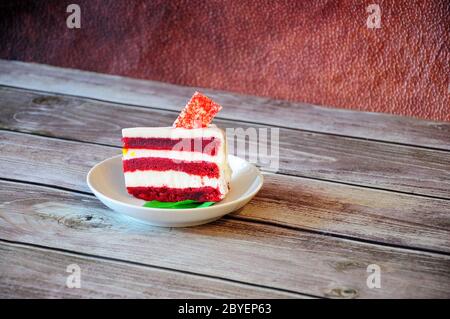 Un morceau de cheesecake en velours rouge décoré de feuilles de menthe sur une plaque blanche se tient sur une table en bois. Gros plan. Banque D'Images