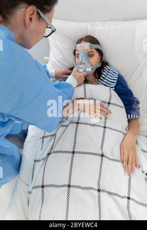 Le médecin contrôle la connexion du ventilateur. L'adolescent est allongé sur un lit d'hôpital. Masque à oxygène sur les voies respiratoires. Banque D'Images