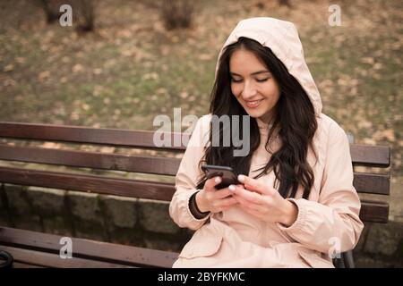 jour de pluie dans le parc, une fille assise sur un banc et utilisant un téléphone cellulaire Banque D'Images