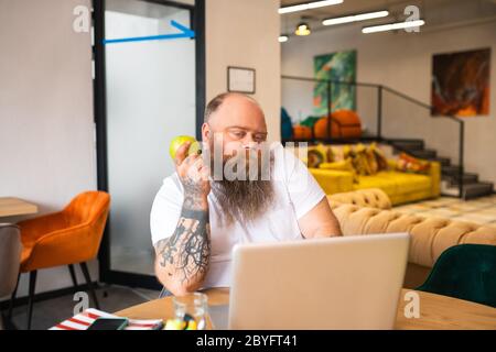 Homme barbu chauve en t-shirt blanc regardant quelque chose en ligne Banque D'Images