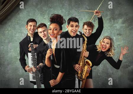 Groupe de musique internationale gaie sur fond de mur gris, un groupe de musiciens posant sur la caméra dans les mains de divers instruments, guitares Banque D'Images