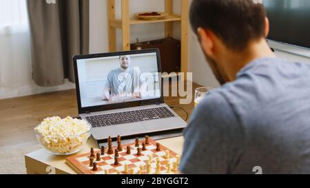 Heureux meilleurs amis jouant aux échecs sur appel vidéo pendant la quarantaine du coronavirus. Boire de la bière et manger du pop-corn. Banque D'Images