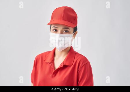 Femme de livraison portant une casquette rouge et un masque de protection contre le coronavirus avec un sourire heureux et frais sur le visage. Personne chanceux. Banque D'Images