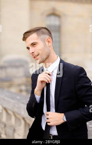 Portrait de jeune caucasien de la cravate redressante et portant le costume noir. Banque D'Images