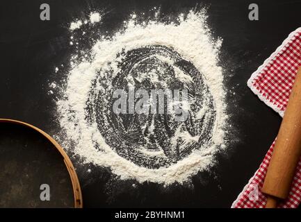 farine de blé blanc dispersée sur une table noire et une rollpin brun très ancienne, grille ronde, vue de dessus Banque D'Images