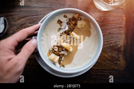 Manger un bol de petit déjeuner. Yaourt, fraise, bleuet, graines, noix de coco, fruits frais et secs dans un bol en céramique blanc dans les mains. Manger propre, manger Banque D'Images