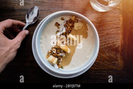 Manger un bol de petit déjeuner. Yaourt, fraise, bleuet, graines, noix de coco, fruits frais et secs dans un bol en céramique blanc dans les mains. Manger propre, manger Banque D'Images