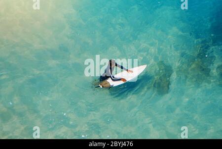 Jeune surfeur sportif qui porte sa planche à surf et qui va à la vue sur l'océan. Riche belle couleur eau comme un fond pour le blog de voyage ou site Web. Banque D'Images