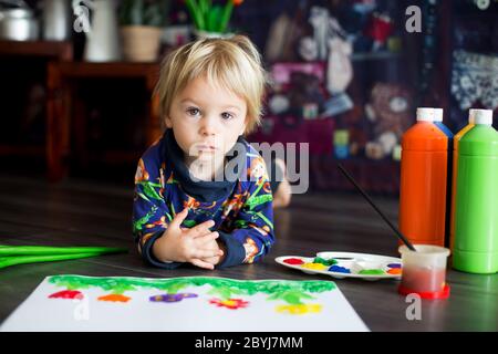 Doux tout-petit blond enfant, garçon, peinture avec des couleurs, petits poussins qui marchent autour de lui, faisant des imprimés amusants sur son papier Banque D'Images