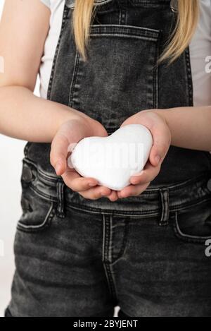 Petite fille tenant un coeur blanc dans ses mains. La fille se tient sur un fond blanc isolé Banque D'Images