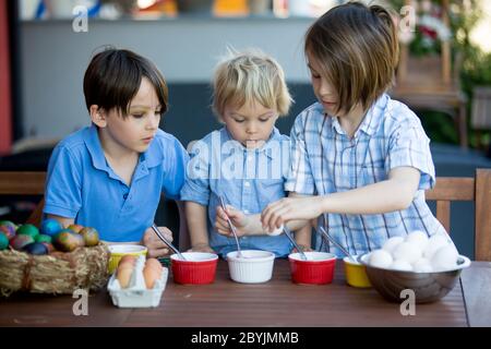 Enfants doux, frères, coloration et ponte des œufs pour Pâques dans le jardin, à l'extérieur à la maison dans l'arrière-cour Banque D'Images