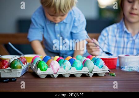 Enfants doux, frères, coloration et ponte des œufs pour Pâques dans le jardin, à l'extérieur à la maison dans l'arrière-cour Banque D'Images