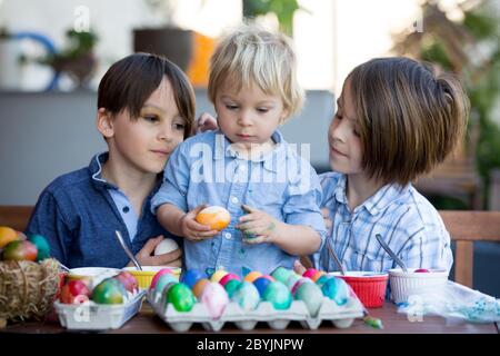 Enfants doux, frères, coloration et ponte des œufs pour Pâques dans le jardin, à l'extérieur à la maison dans l'arrière-cour Banque D'Images