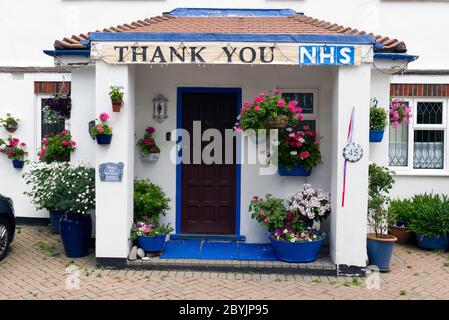 Un panneau disant Merci NHS suspendu au-dessus du porche d'une maison de banlieue avec des paniers suspendus colorés dedans. Sud-Ouest de Londres. Banque D'Images