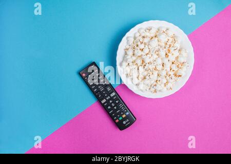 Bol de pop-corn blanc sur fond bleu et violet avec télécommande noire pour téléviseur Banque D'Images