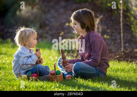 Enfants adorables, manger des lapins de chocolat et se battre avec des œufs de pâques après la chasse aux œufs dans le jardin au coucher du soleil Banque D'Images