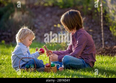 Enfants adorables, manger des lapins de chocolat et se battre avec des œufs de pâques après la chasse aux œufs dans le jardin au coucher du soleil Banque D'Images