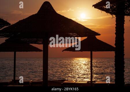 Le lever du soleil à travers des parasols tissés et des chaises longues. Sur la plage surplombant la mer Rouge, Charm el-Cheikh. Banque D'Images