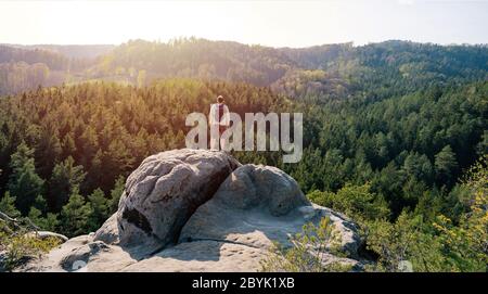 Randonneur avec sac à dos pour se détendre au sommet d'une roche de grès et profiter de la vue sur la vallée au lever du soleil Banque D'Images