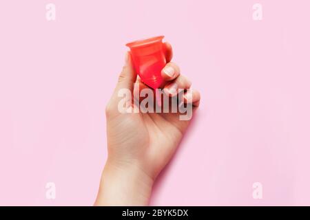 Woman's hand holding coupelle menstruelle sur fond rose. La santé de la femme et de produits d'hygiène féminine écologique concept. Banque D'Images