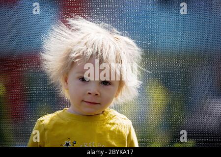 Cute little boy avec électricité statique des cheveux, avoir son portrait pris à l'extérieur sur un trampoline Banque D'Images