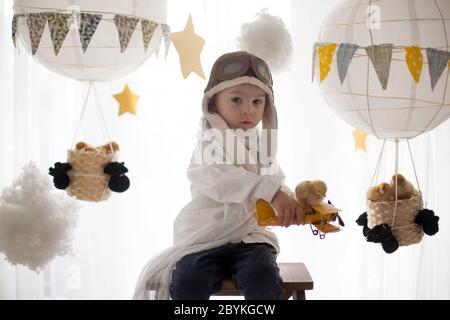 Mignon petit enfant, garçon, jouant avec des poussins à la maison, prétendant qu'il vole dans le ciel, pilote avec avion et poussin d'animal de compagnie Banque D'Images