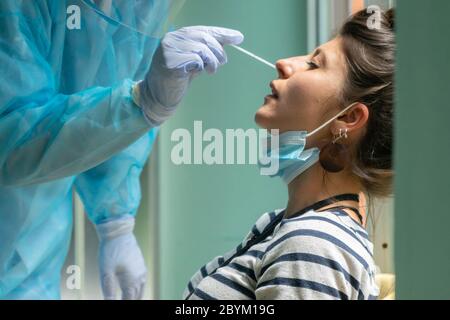 Un professionnel de la santé doté d'un équipement de protection effectue un écouvillon de coronavirus sur une fille caucasienne.écouvillon de nez pour Covid-19. Banque D'Images