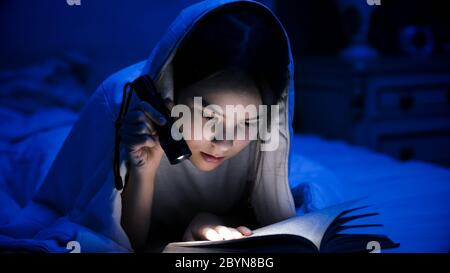 Portrait d'une adolescente lisant un livre au lit avec lampe de poche Banque D'Images