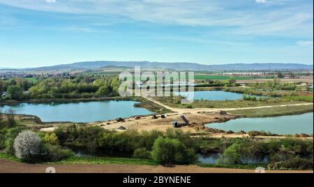 Vue aérienne de plusieurs étangs dans une zone d'extraction de sable avec une rivière en premier plan et des montagnes à l'horizon Banque D'Images