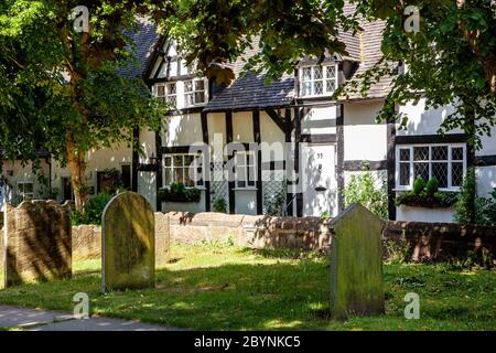 Vue sur les chalets de campagne noirs et blancs à travers les pierres tombales de chantier de l'église du village de Sainte Marie et tous les saints Grand Budworth Cheshire Banque D'Images