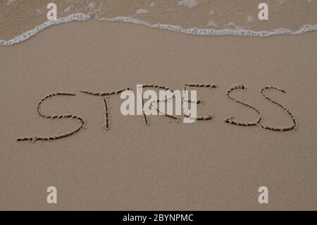Texte de stress inscrit dans le sable avec l'eau venant Banque D'Images