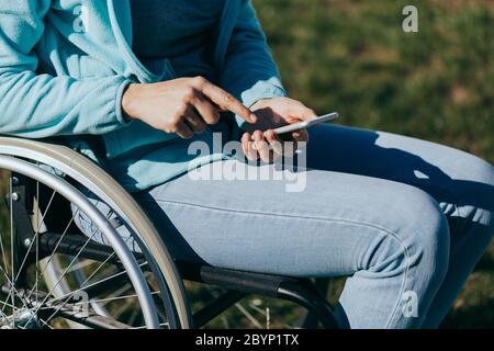 Une femme en fauteuil roulant avec un téléphone dans sa main marche dans la rue, sa main est proche, une méconnaissable Banque D'Images