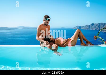 Couple en vacances de luxe en Grèce, Oia Santorini hommes et femme à la piscine à débordement de caldera donnant sur l'océan de l'île de Santorini Banque D'Images