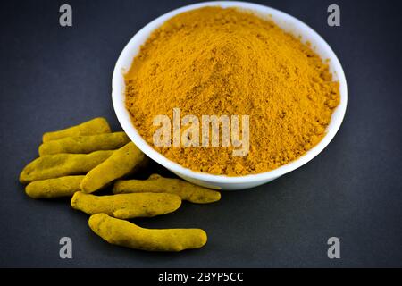 Poudre curcuma dans un bol blanc avec racines ou écorces Banque D'Images