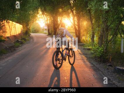 Femme à vélo sur la route rurale au coucher du soleil en été
