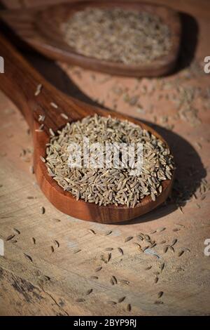 Graines de cumin en cuillère en bois sur fond en bois Banque D'Images