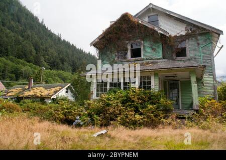 Maison abandonnée couverte de feuillage dans la ville fantôme d'Ocean Falls, dans la forêt tropicale de Great Bear, Colombie-Britannique, Canada. Banque D'Images