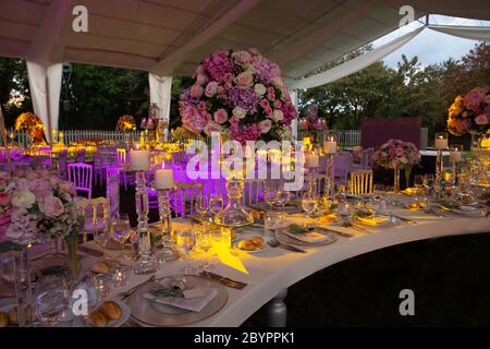 Une réception de mariage en plein air de luxe, en plein air, à la campagne, avec chaises tiffany rustiques blanches, arrangements de fleurs sur la table, pièces centrales en cristal et b Banque D'Images