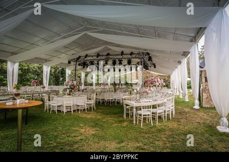 Une réception de mariage en plein air de luxe, en plein air, à la campagne, chaises tiffany rustiques blanches, arrangements de fleurs sur la table, pièces centrales en cristal, bateau Banque D'Images