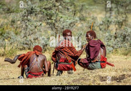 Trois jeunes guerriers Masai en vêtements et armes traditionnels sont assis dans la savane. Tanzanie, Afrique de l'est, 12 août 2018. Banque D'Images