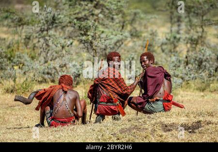 Trois jeunes guerriers Masai en vêtements et armes traditionnels sont assis dans la savane. Tanzanie, Afrique de l'est, 12 août 2018. Banque D'Images