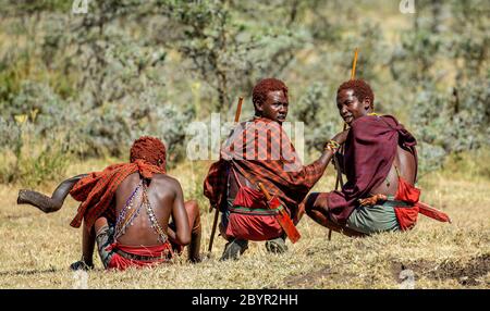 Trois jeunes guerriers Masai en vêtements et armes traditionnels sont assis dans la savane. Tanzanie, Afrique de l'est, 12 août 2018. Banque D'Images