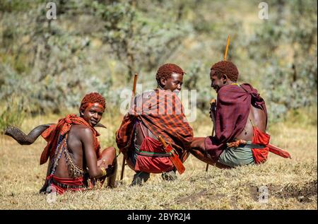 Trois jeunes guerriers Masai en vêtements et armes traditionnels sont assis dans la savane. Tanzanie, Afrique de l'est, 12 août 2018. Banque D'Images